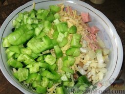 Вкусный салат: Добавляем очищенные и порезанные кубиками огурцы, порезанную кубиками колбасу, натертый на крупной терке сыр, порезанный колечками зеленый лук и мелко порезанный чеснок.
