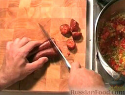 Картофель по-риохски: Колбаски чоризо нарезать кружочками. Всыпать в кастрюлю.