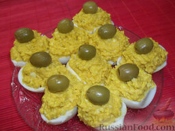 Яйца, фаршированные икрой минтая и плавленым сыром: Сверху украсьте фаршированные яйца оливками.  Яйца, фаршированные икрой минтая, готовы, можно подавать.