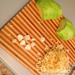 Свинина с авокадо под сырной шапкой: Авокадо почистить, вытащить косточку, нарезать полукольцами. Сыр натереть на крупной терке. Чеснок порезать пластинками.