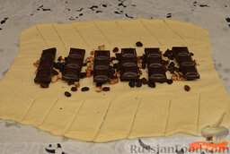 Пирог с шоколадом: Раскатать тесто в тонкий пласт, сделать надрезы по бокам.  Выложить горсть орехов и изюма.  Выложить шоколад.
