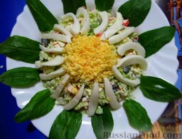 Салат из пекинской капусты и крабовых палочек "Ромашка": Желтки выложите в центр в виде круга, а по краям выложите полоски белка. Украсьте салат зелеными листочками.