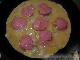 Омлет с колбасой: Добавить яйца, установить маленький огонь, с помощью лопатки поддевать середину яйца, чтобы все равномерно пропеклось. Закрыть крышкой и жарить до готовности.