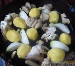 Кролик, запеченный с овощами: Переложите обжаренного кролика на тарелку, а в ту же сковороду добавьте еще немного масла, разогрейте его и выложите в сковороду целый чищеный картофель, резаные грибы и кусочки лука.